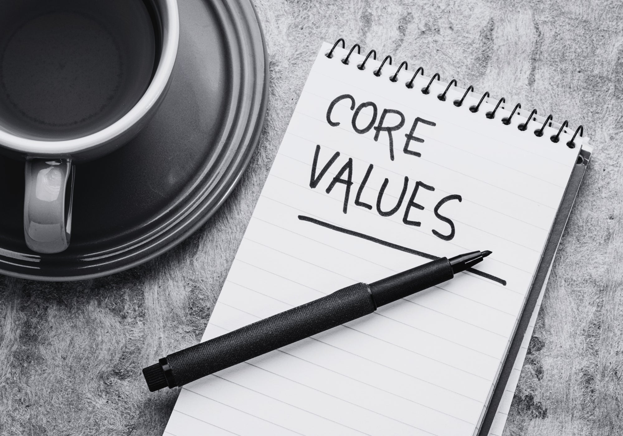 Notepad with 'CORE VALUES' text, pen, and coffee cup on a textured surface