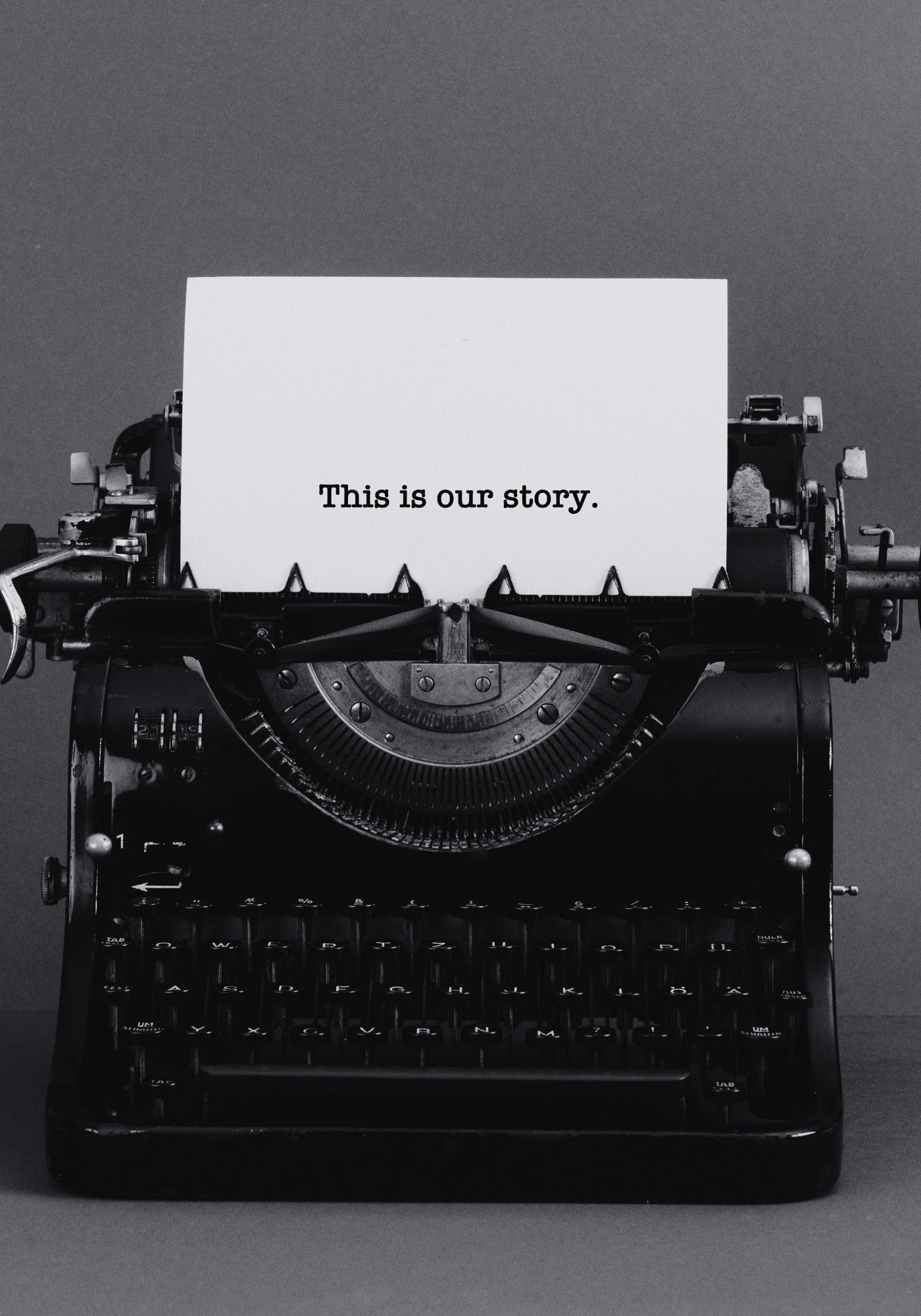 Vintage typewriter with a sheet of paper displaying 'This is our story.' on a gray background