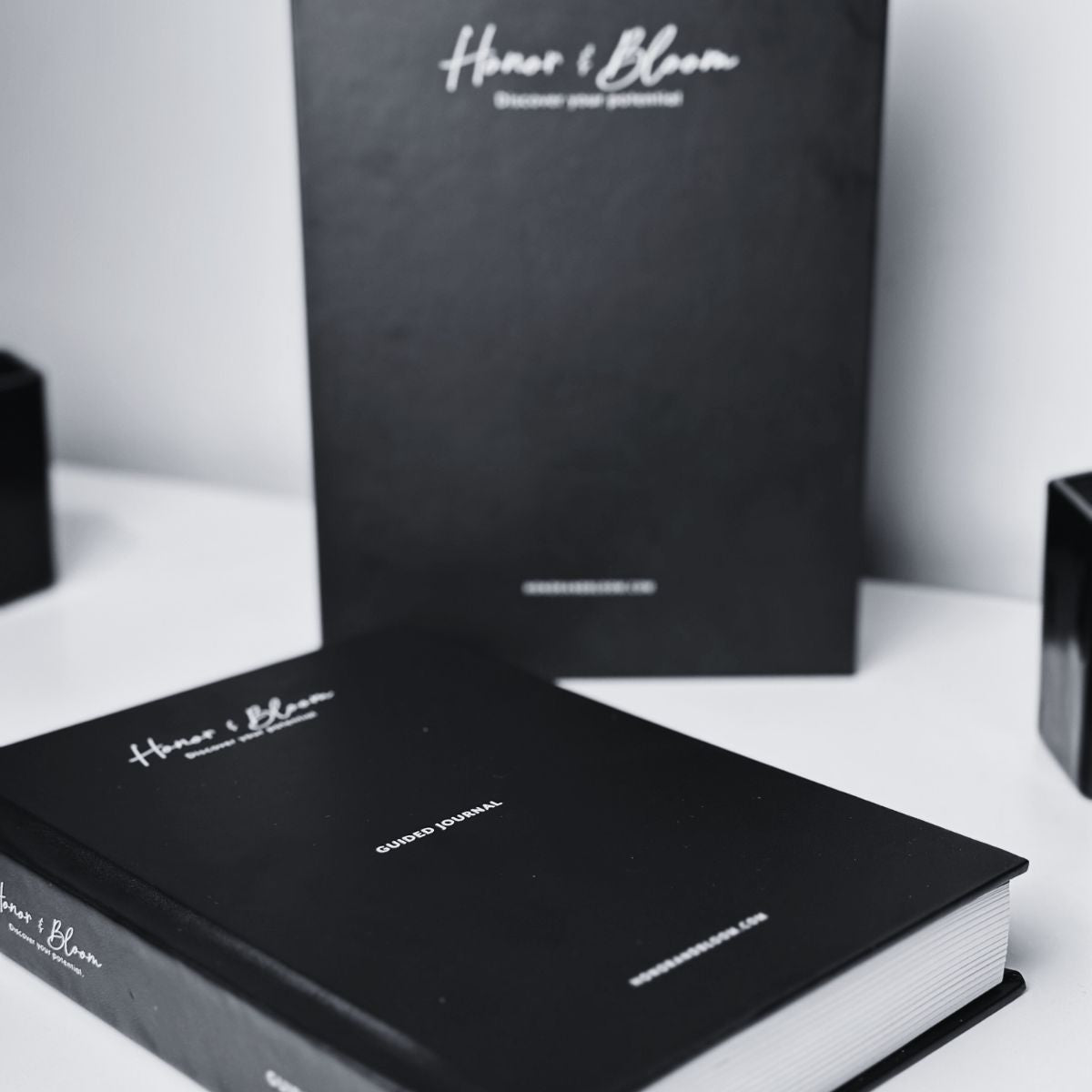 Black books with 'Honor & Bloom' branding on a white surface
