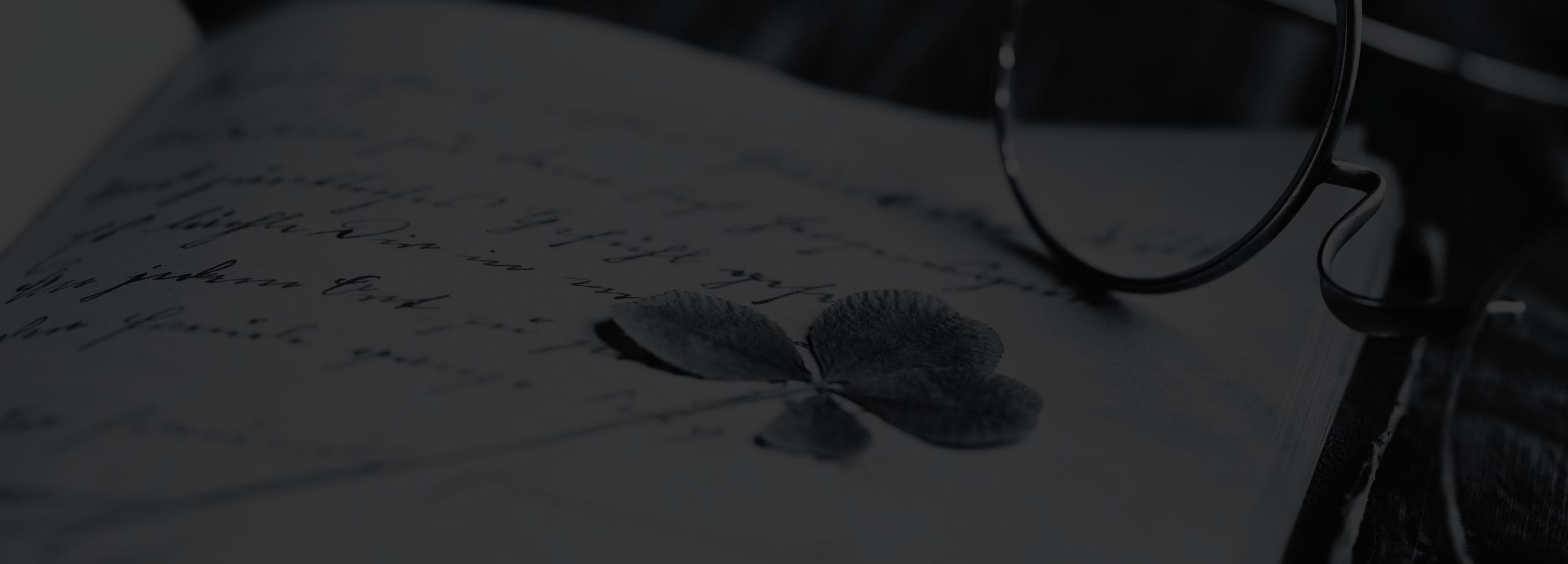 Eyeglasses resting on a book with handwritten text and a four-leaf clover.